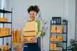© Parichat - Smiling African American entrepreneur holding packages in storehouse