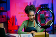 © Parichat - Young african american woman working at her startup small business, recording a video blog about her products