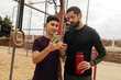 © kleberpicui - Teenage boy and adult man looking at a smartphone together at an outdoor gym
