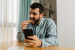 © Novak - Man having a snack and using phone in cozy living room