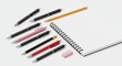 © Maria - Array of pens pencils and eraser arranged next to a spiralbound notebook on a plain white surface