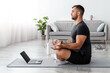 © Prostock-studio - Calm millennial caucasian guy sitting, meditating on mat with laptop in living room interior, profile, copy space. Practice yoga, workout, online lesson and body care at home during covid-19 outbreak