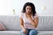 © Prostock-studio - Flu, illness, treated, health care, disease symptoms, covid-19 outbreak. Despaired unhappy millennial african american female on sofa suffering from sore throat in living room interior, free space