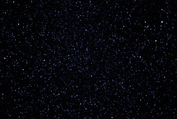 Dark expansive background filled with multitude of tiny, sparkling blue and white stars, suggesting a vast cosmic night sky, or a distant galaxy