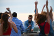 © pressmaster - Group of multiethnic young adults dancing outdoors while Caucasian young adult man DJ operating mixing console, people raising hands and enjoying music at rooftop party