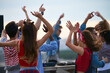 © pressmaster - Group of multiethnic young adults dancing outdoors with raised arms, enjoying music together near DJ booth, diverse men and women moving energetically during rooftop party event