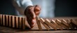 © Green - A hand prevents a row of wooden dominoes from falling on a textured wooden surface against a dark background