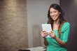 © wavebreak3 - Asian woman smiling and holding white tablet at home office with documents on table, copy space
