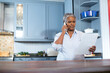 © wavebreak3 - Senior African American woman reading document and holding smartphone at kitchen island, copy space