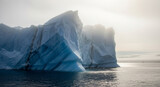 Dramatic iceberg floats serenely in arctic waters under a soft, hazy sky creating a sense of wonder