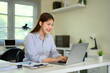 © Prathankarnpap - Smiling young woman working on a laptop in a modern office with natural light