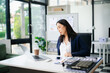 © laddawan - Asian businesswoman stretching arms in office with tired expression, relieving muscle tension from long work hours.
