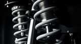 Close-up of a modern automotive suspension system, featuring a grey coil spring and silver shock absorber on a dark background. Essential for vehicle stability and ride comfort.