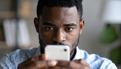 Intense young African man stares at his smartphone screen with a serious and focused expression, consumed by digital content or a concerning message
