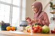 © Art_Photo - Muslim woman happy cooking healthy meal in kitchen wearing hijab making soup in pot with fresh vegetables food preparation activity nutrition, ramadan healthy recipe preparation, islamic food culture