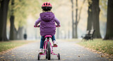 Little girl riding pink bike in autumn park wearing helmet enjoying outdoor activity child safety