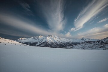Wall Mural - Winter view of rugged mountains with snowy summits and a grassy field under a moody cloudy sky