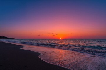 Wall Mural - scarlet twilight above a shadowy shore and ocean with limited water view and scattered small clouds 