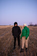 © Niko_Dali - Two friends share a moment in a tranquil field at dusk, enveloped in chilly air while dressed warmly for the winter weather, illuminating their bond through conversation