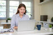 © matinee - Smiling young businesswoman working at desk with laptop and financial documents in modern office.