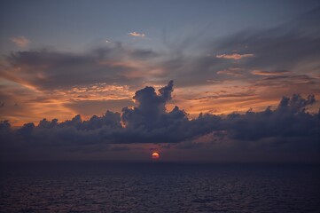 Wall Mural - twilight clouds above ocean at sundown with vibrant orange horizon