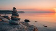 © Erni - Rock cairn on larger boulder by water at sunset; warm, orange hues