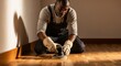 © Alla - A middle-aged Black man, around 40, wearing work trousers, gloves, and a cotton shirt, carefully polishing parquet flooring with circular hand motions