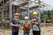 © skarie - Group of engineers and architects wearing safety helmets giving thumbs up at construction site with scaffolding background.