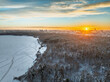 Snow-covered forest on lake shore with ice at sunset and the city on horizon, auerial view