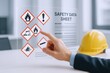 © The Little Hut - Safety Data Sheet (SDS) Review on Transparent Display with Hand Pointing to Hazard Symbols and Hard Hat