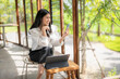 © Apichat - woman is sitting at a table with a laptop and a cell phone