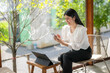 © Apichat - woman is sitting on a chair with a laptop and a cell phone in front of her
