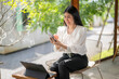 © Apichat - woman is sitting in a chair with a laptop and a cell phone in front of her