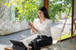 © Apichat - woman is sitting on a chair with a laptop and a cell phone in front of her