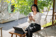 © Apichat - woman is sitting on a chair with a laptop and a cell phone in front of her