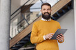 © Dusan Petkovic - Bearded Business Professional in Sweater Working with Tablet Device Near Modern Staircase
