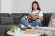 © Pixel-Shot - Beautiful young woman reading book and sitting on black sofa at home