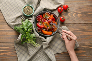 Wall Mural - Female hand with fork and bowl of fresh tomato salad on wooden background