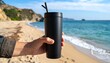 © Dea - Handheld black tumbler on beach