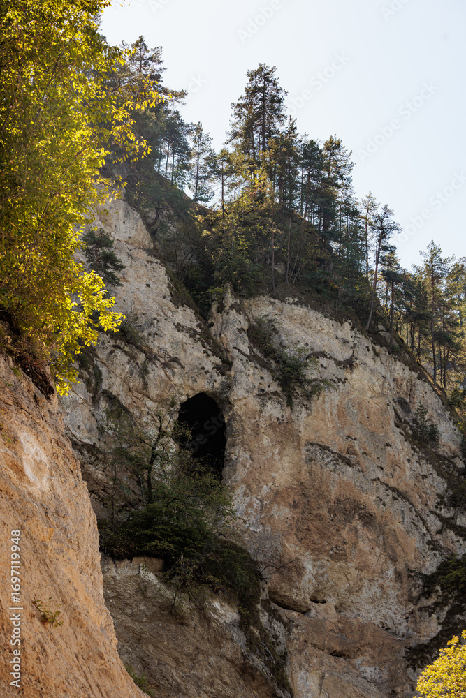 Rocky cliffs with tree-covered slopes and natural caves. Bright sunlight illuminates the scene.