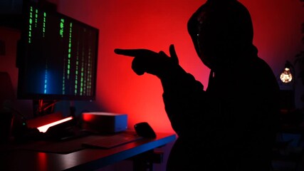 hooded hacker sits in front of a monitor and wears a coat to hack into security systems and access personal information in a neon-lit computer room.