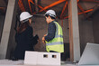© ARMMY PICCA - Construction manager and engineer dressed in orange work vests and hard helmets explore construction documentation on the building site near the steel frames