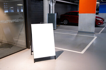 Wall Mural - Blank white mockup signboard placed in an indoor parking garage, with cars parked in the background. Empty board with copy space for advertising, signage, branding, and urban infrastructure.