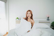 © WMSTUDIO - Young woman smiling while sitting on a cozy bed with white linens in a bright and airy bedroom filled with plants and soft natural light
