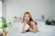 © WMSTUDIO - Smiling Young Woman Relaxing in Bed with Soft White Sheets in Modern Bedroom with Natural Light and Green Plants in Background