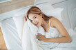 © WMSTUDIO - Smiling woman in white bed with soft pillows and cozy blanket looking happy, enjoying morning and relaxation with natural light in modern bedroom