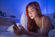 © WMSTUDIO - Young Woman Relaxing in Bed While Using Smartphone at Night with Soft Blue Lighting in Cozy Bedroom Environment