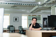 © fotolite - A young man sits at a desk in a computer lab or office, leaning his face on his hand with a frustrated or tired expression. Empty room shows sense of isolation or burnout.