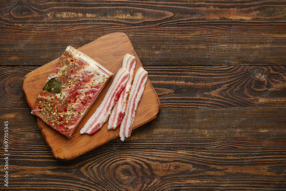 Slices of seasoned bacon on a wooden cutting board for preparation and cooking