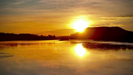 Wall Mural - Drone view of a glowing golden sunset casting warm light across a wide calm lake